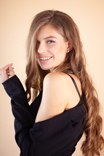 Young girl with a beautiful smile and braces on her teeth. Portrait of a beautiful young girl with a cheerful smile and long curly hair, set against a beige background.