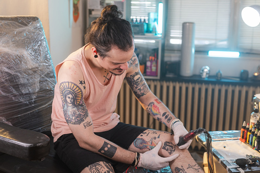 Shot of a male tattoo artist tattooing himself. He is drawing a tattoo on his leg.