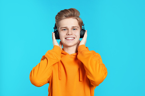 Teenage boy listening to music with headphones on light blue background