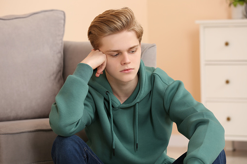 Upset teenage boy sitting alone in room