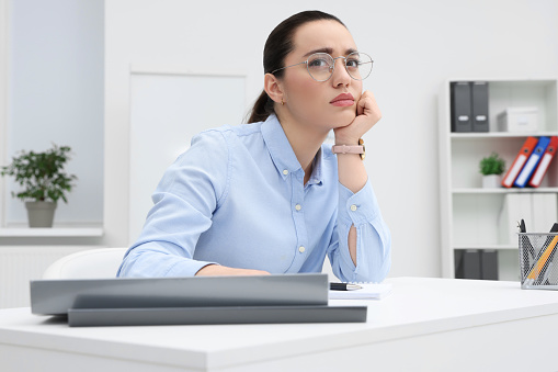 Unhappy young female intern at table in office