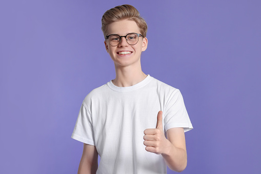 Teenage boy showing thumb up on purple background