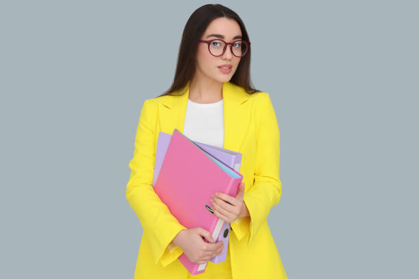 istock Young female intern with eyeglasses and folders on grey background 1810224666
