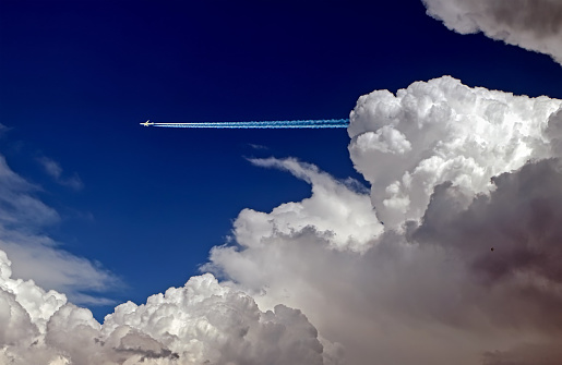 A distant passenger jet flies out from behind a cloud