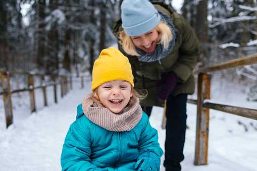 Close up shot of a cute little girl playing with her mother and enjoying a day outside in the snow, looking down and smiling. They are dressed in winter clothes.