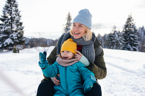 Close up shot of a beautiful women and her cute little  daughter in winter clothes and snowsuits, smiling while enjoying spending a day outside in the snow.