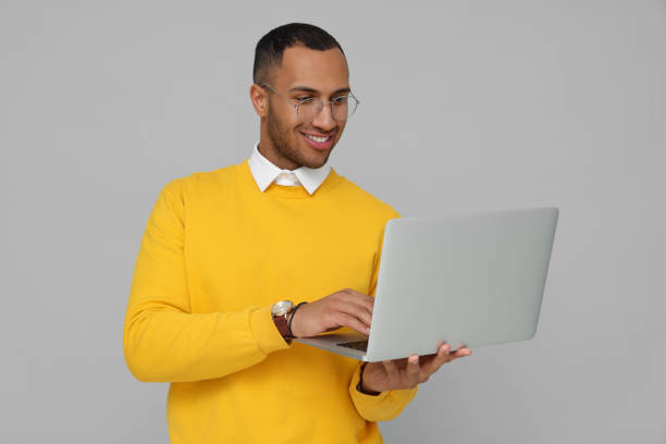 istock Happy young intern working on laptop against light grey background 1810256185