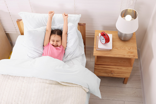 Cute little girl stretching in cosy bedroom, above view