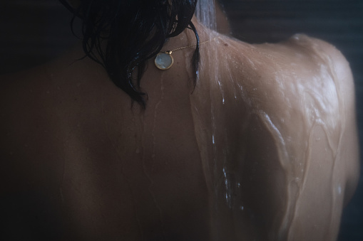 rear view of back of mature middle-eastern adult woman in the shower with hot water running over her skin.relax, wellness and wellbeing concept.