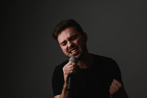 magician beginning performance, speaking to an audience with a microphone. man in black suit with colourful make-up on face isolated over red background