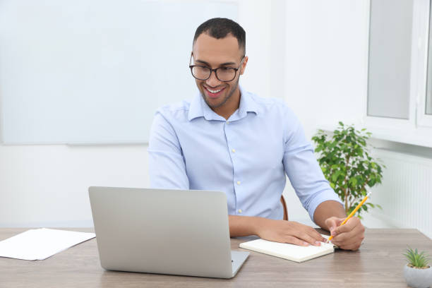 istock Happy young intern working with laptop at table in modern office 1810300497