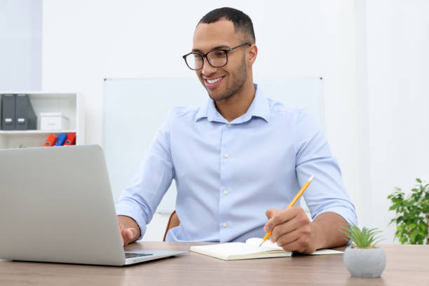 istock Happy young intern working with laptop at table in modern office 1810308523