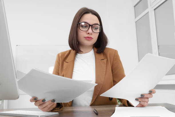 istock Puzzled young intern with paper sheets at table in modern office. First work day 1810311204