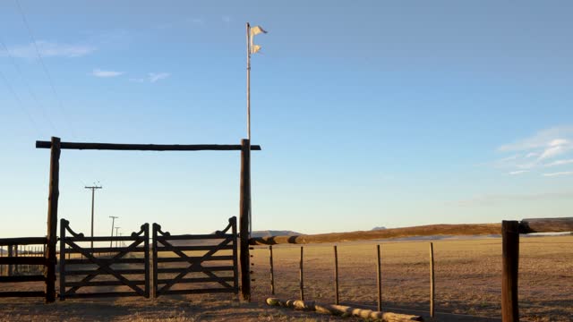 Entrance to a rural establishment formed by a gate and wooden logs. Remains of a flag flying. 4K Horizontal.