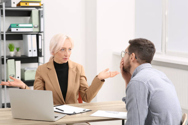istock Boss and stressed employee discussing work issues at wooden table in office 1810324321