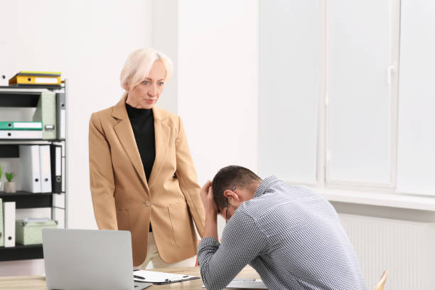 istock Boss and stressed employee discussing work issues at wooden table in office 1810324826