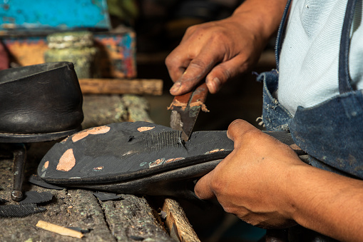 A shoemaker with a long career repairing shoes, changes soles, mends and places insoles on behalf of his clients, in an establishment with widely used tools and where he has been working for many years.