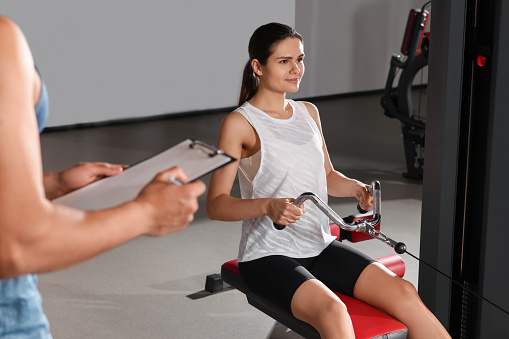 Woman doing exercise in modern gym while trainer looking at workout plan