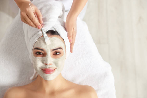 istock Cosmetologist applying mask on woman's face in spa salon, top view. Space for text 1810420284
