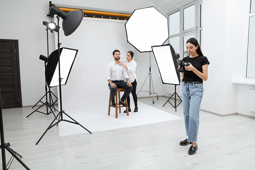Professional photographer and stylist working with model in modern photo studio