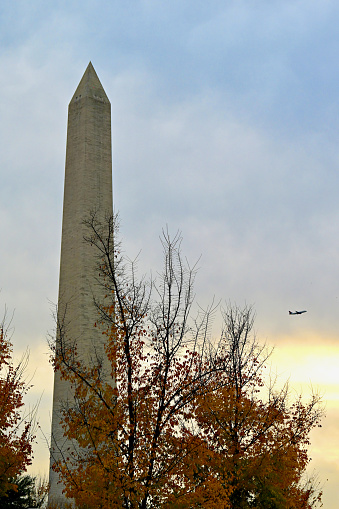 Washington, D.C., USA - November 20, 2023: A regional jet taking off from Ronald Reagan National Airport flies behind the Washington Monument on a late autumn afternoon as the sun sets in the background.