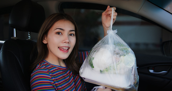 Image of Young Asian woman shows a bag of food while in the car. Women friends fun joy relax enjoy a Thai meal. Lifestyle, People and Thai food concepts.