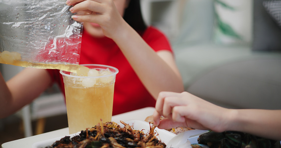 Image of Young Asian woman eating Thai food and drinking longan juice while sitting on the floor at home. Women friends fun joy relax enjoy a Thai meal. Lifestyle, People and Thai food concepts.
