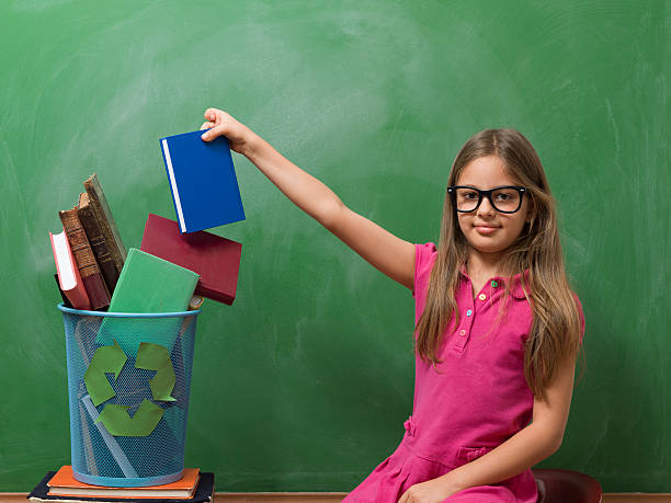 Little girl leaving book in recycling bin before blackboard