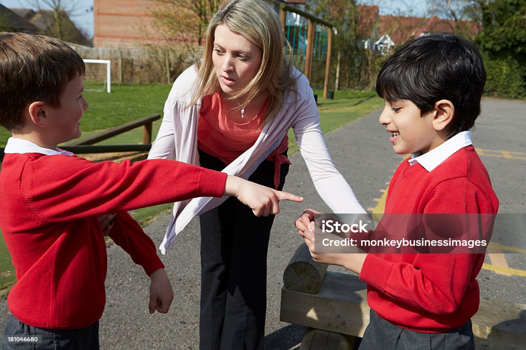 Insegnante interruzione di due ragazzi lottare In Parco giochi - Foto stock royalty-free di Lottare