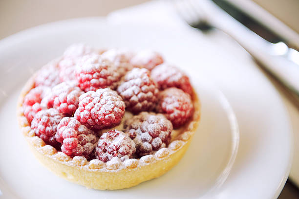Fresh gourmet raspberry tart dusted with powdered sugar on a plate at authentic French cafe