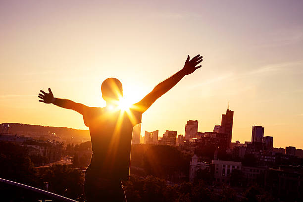 Young man with arms raised in front of the city skyline.