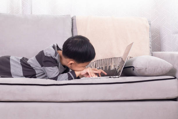 istock Asian happy boy kid lying down on sofa watching video games interested technology laptop, cheerful children lifestyle holiday at home addict computer, remote homeschool education digital learning 1810478155