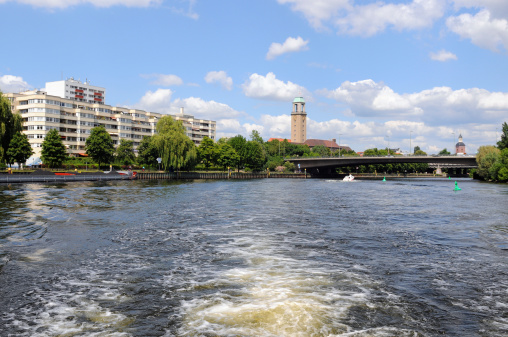 Town hall of Spandau, district of Berlin (Germany). In Foreground Havel Riverwith Barge at River Station. Houses and a promenade at Havel River.
