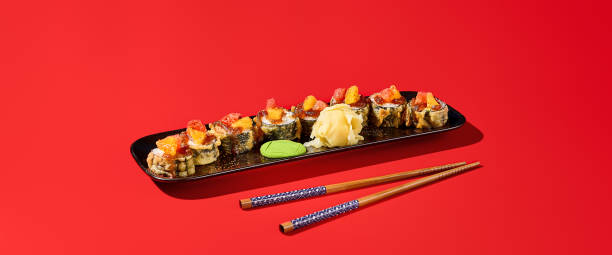 rolo de sushi tempura preparado na hora, coberto com molho cítrico. retratado contra um dramático pano de fundo vermelho com sombras ousadas. banner com espaço para cópia - 16626 - fotografias e filmes do acervo