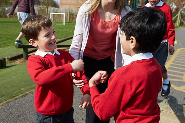 Teacher Stopping Two Boys Fighting In Playground Female Teacher Stopping Two Boys Fighting In Playground schoolyard fight stock pictures, royalty-free photos & images