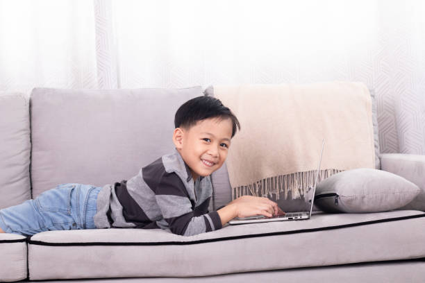 frère asiatique petit garçon jouant à un jeu seul à la maison allongé sur le canapé à l’aide de la technologie moderne sans fil dépendance à l’ordinateur portable, fils mignon étudiant l’école à la maison tapant au clavier regardant la le - 5510 photos et images de collection