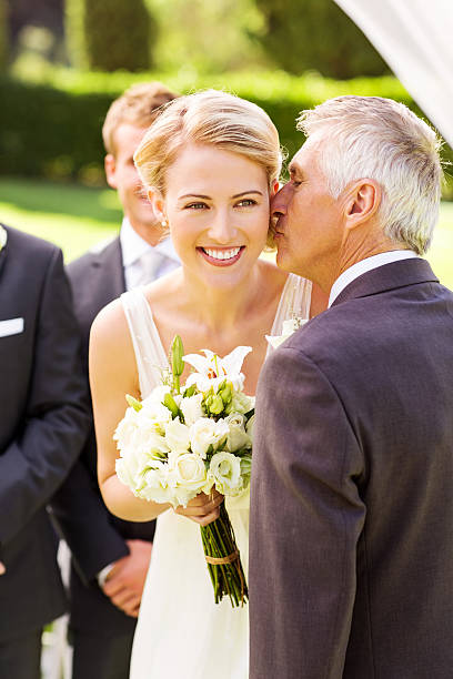 Bride Looking Away While Father Kissing Her On Cheek