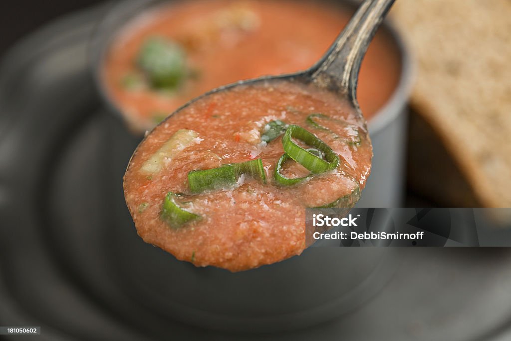 Bite Of Gazpacho Soup A high angle close up shot of a spoonful of gazpacho with a pewter cup full of soup and bread in the background. Biting Stock Photo