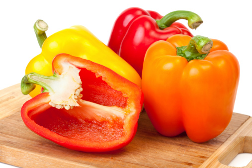 Three and a half yellow, red and orange bell peppers on a cutting board against a white background.