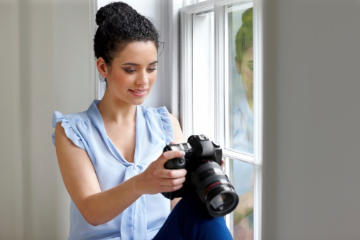Image of attractive young female watching pictures on camera by a window