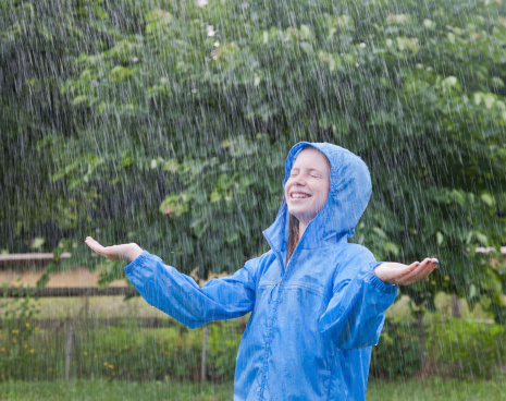 Confident smiling young girl enjoying a pouring rainfall in the backyard