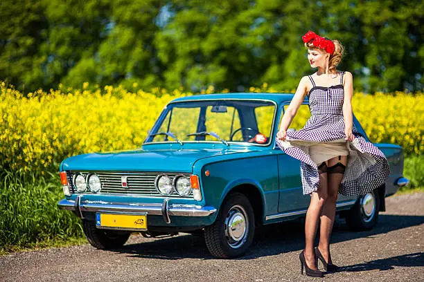 Beautiful young woman posing with old Polish (Italian) car in rural scenery.