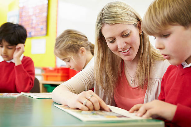 mężczyzna nauczyciel pomaga źrenica z czytanie na biurko - elementary student school uniform uniform education zdjęcia i obrazy z banku zdjęć