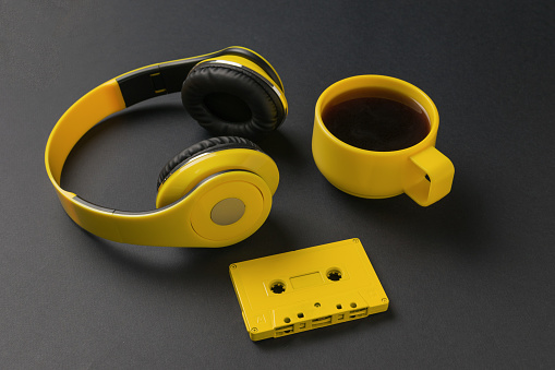Coffee in a yellow glass, headphones and a cassette on a black background. The concept of a stylish workplace.