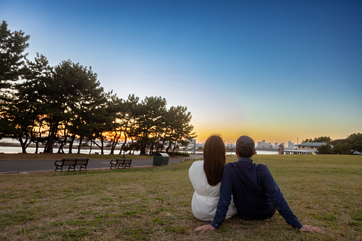 Couple sitting together on grass in seaside park at sunset time