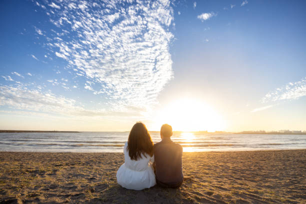 istock Couple on the beach at sunset - sitting together 1810576950