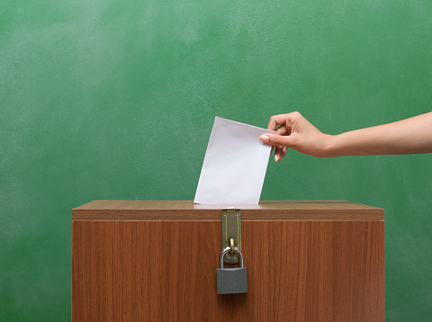 Poll Envelope In Human Hand Inserting To The Ballot Box  in front of black blackboard for election