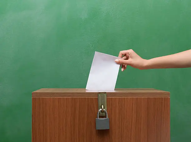 Poll Envelope In Human Hand Inserting To The Ballot Box  in front of black blackboard for election