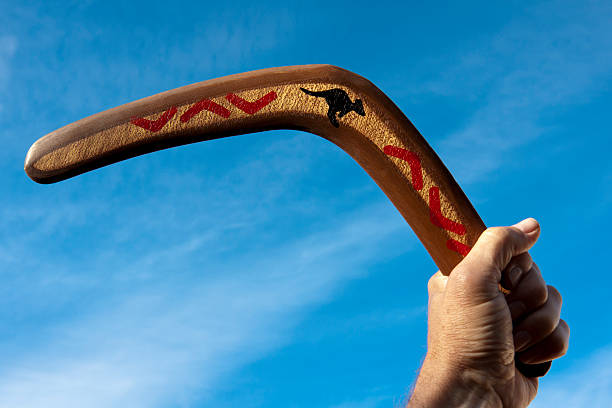 Boomerang held in hand Boomerang being held on a sunny day with some cirrus clouds. boomerang stock pictures, royalty-free photos & images