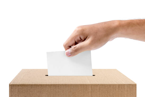 Human hand inserts vote paper into ballot box isolated over white background. Election concept